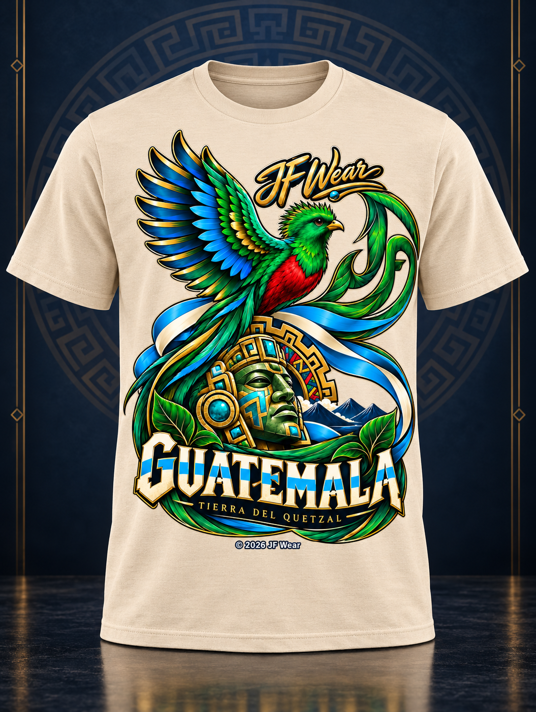 A cream-colored short-sleeve t-shirt featuring a large, colorful graphic print of a Guatemalan quetzal bird, a golden mask, and the text 'JF Wear' and 'GUATEMALA TIPICA DEL QUETZAL'.