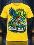 A bright yellow short-sleeve t-shirt featuring a large, colorful graphic print of a Guatemalan quetzal bird, a stone face, and the text 'IF Wear' and 'GUATEMALA' on the front, displayed against a dark blue background with a subtle circular pattern.